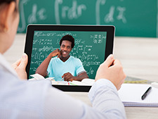 Person looks at tablet with person on screen in front of chalkboard