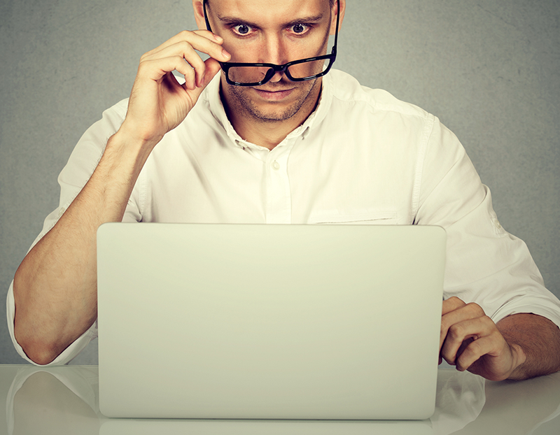 Man looks at computer with eyes raised and holds glasses on the tip of his nose