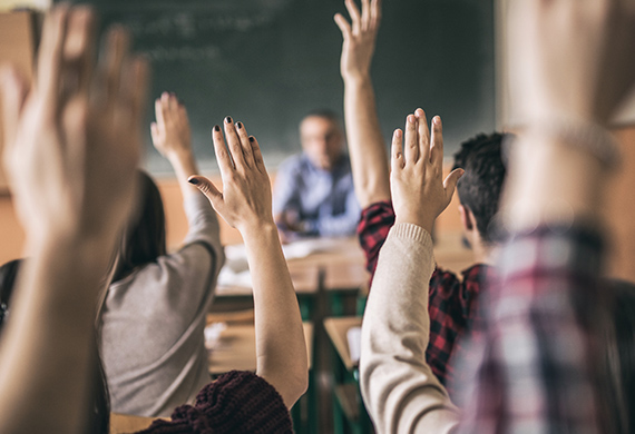 All students have hands raised in classroom for face-to-face teaching