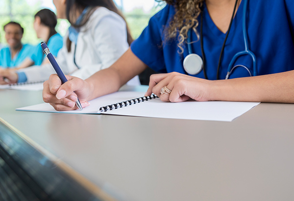 Nursing students with stethoscopes and scrubs take written exam