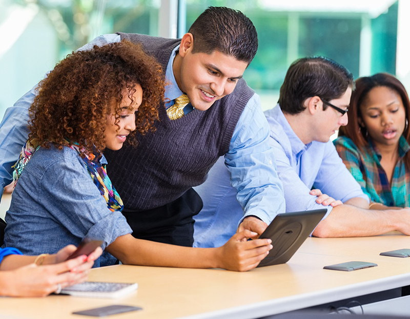 Teacher leans over student to point to opened laptop