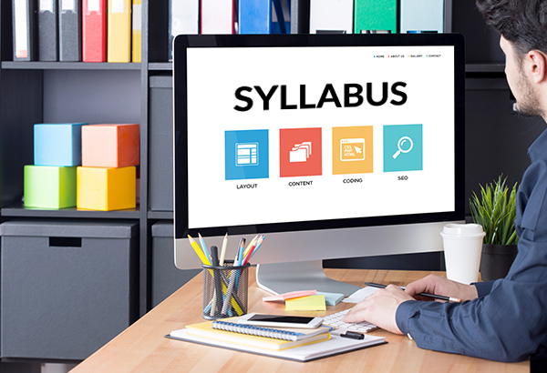 Person looks at computer screen in office with the word, "Syllabus" on the computer screen