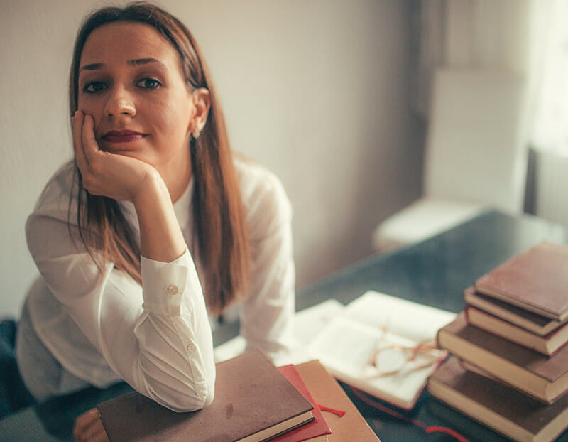 Person rests head in hand with stack of books in front of her