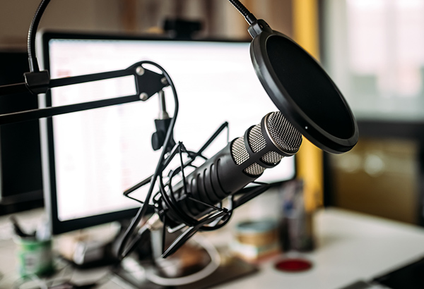 Podcast microphone is setup in front of computer screen and studio