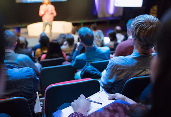 People sit in theater while listening to TED talk presentor