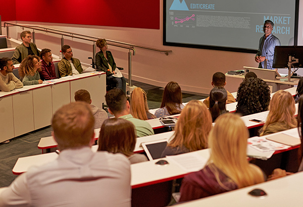 Large lecture hall filled with students look at project in front with instructor