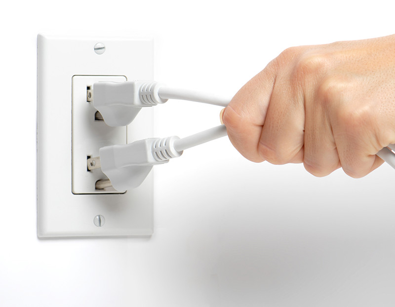 Person's hand unplugs two electrical cords from outlet