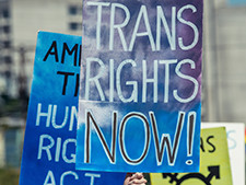 Trans Rights Now! signs are held up in protest for