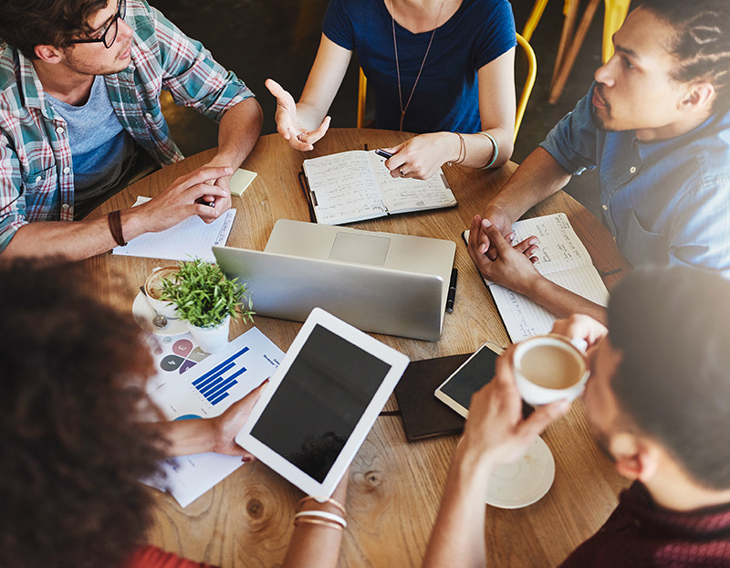 Students collaborate around table with coffee, computers, and notes