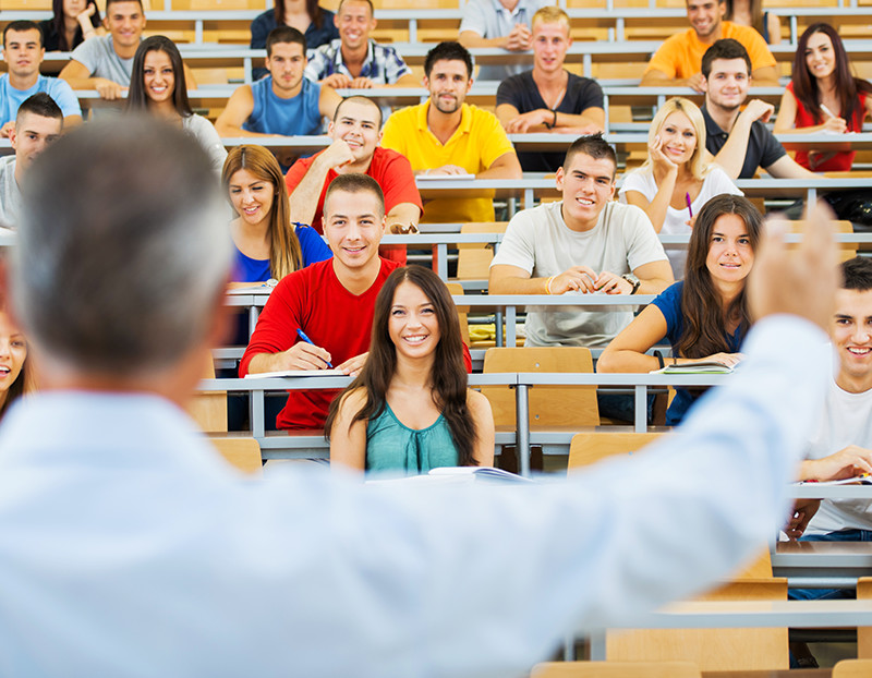 Instructor teaches class in front of large lecture hall full of students