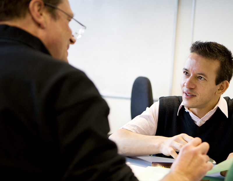 Two faculty member talk with one another at table about a faculty mentoring program