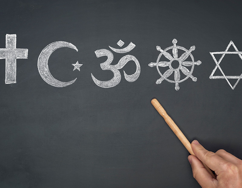 Symbols from different religions are displayed on chalkboard with someone pointing to them
