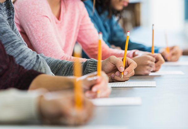 Students line the table with pencils in hand ready to take an exam