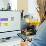 Person looks at phone in hand and calendar events on computer