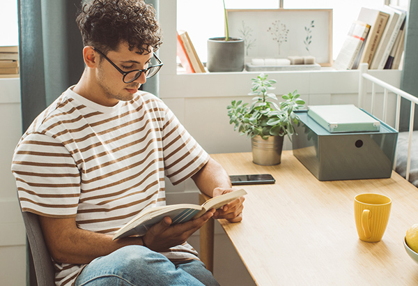 young-man-with-glasses-reading-book-engaged-at-desk