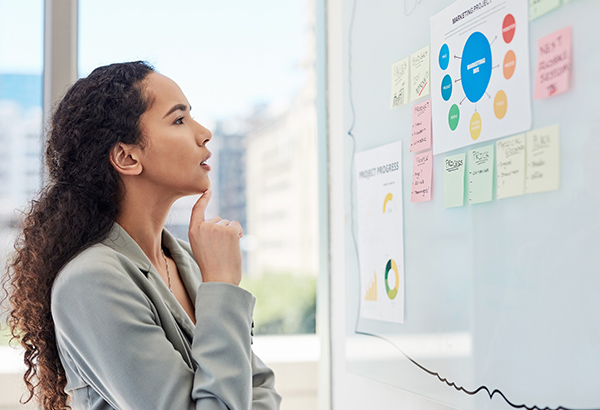 woman-thinking-hard-in-front-of-board-with-different-graphs-and-notes-on-it