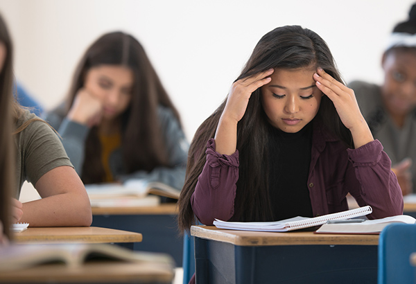 woman-in-classroom-at-desk-eyes-closed-frustrated-looking-down-at-book