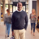 black-man-with-briefcase-smiling-standing-in-middle-of-students-walking-past