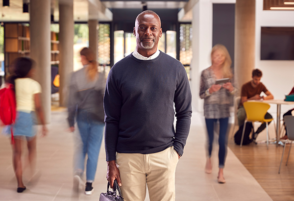 black-man-with-briefcase-smiling-standing-in-middle-of-students-walking-past