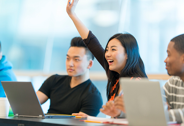 female-student-in-classroom-at-desk-happily-raising-hand