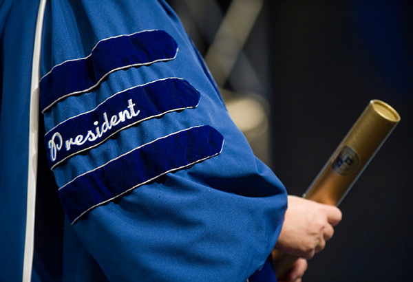 person-wearing-cap-and-gown-that-says-president-holding-a-diploma