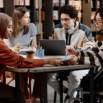 students-in-library-sitting-at-desk-using-laptop-talking