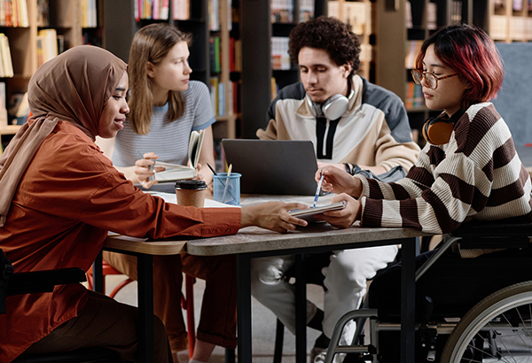 students-in-library-sitting-at-desk-using-laptop-talking