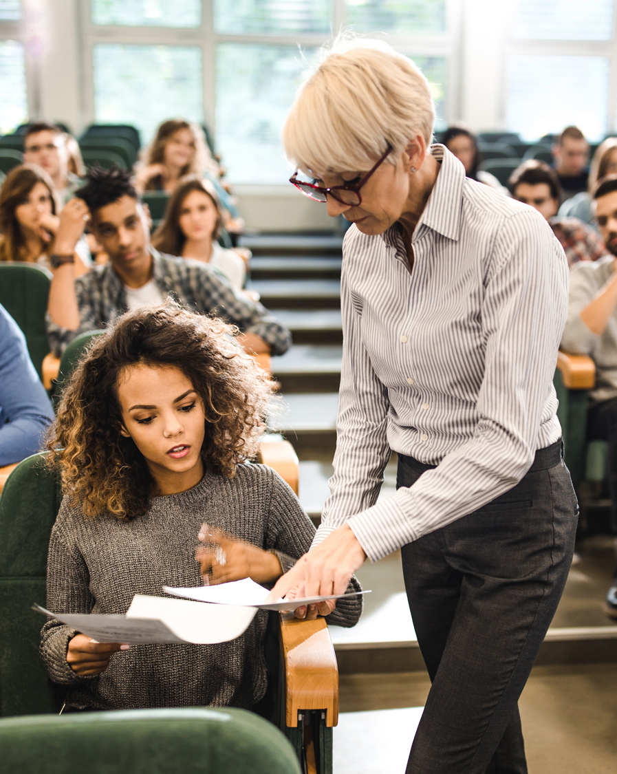 a female professor looking at papers with a student in a lecture hall
