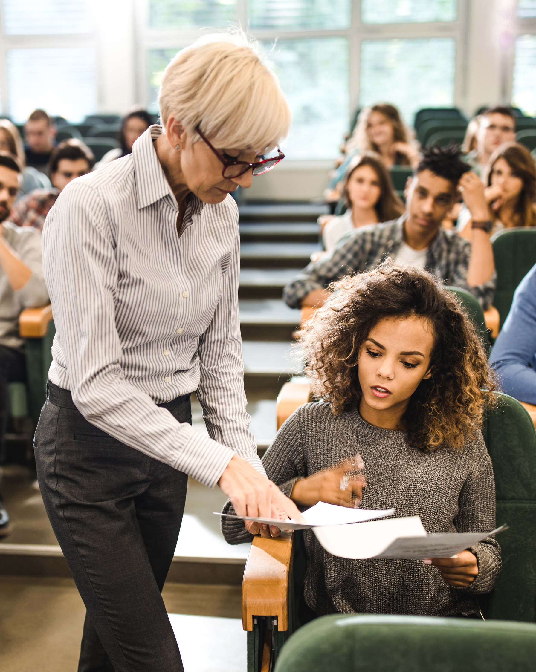 a female professor looking at papers with a student in a lecture hall