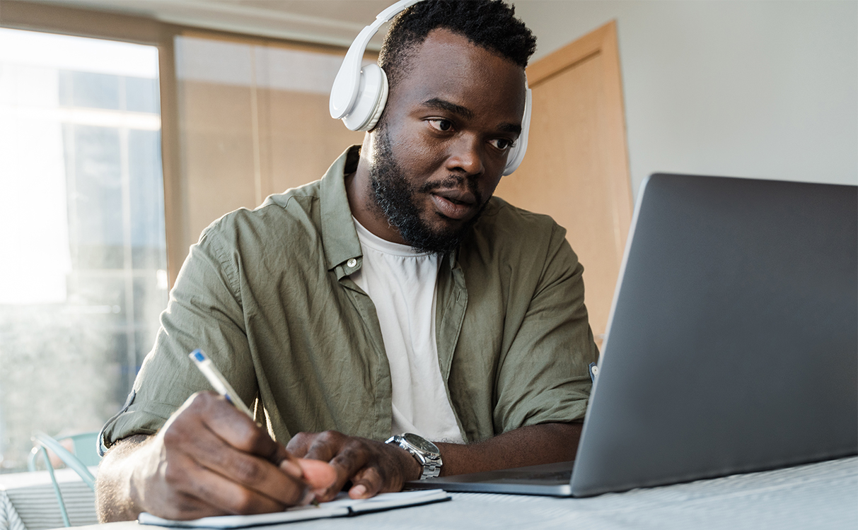 man wearing headphones and watching videos on a laptop while taking notes